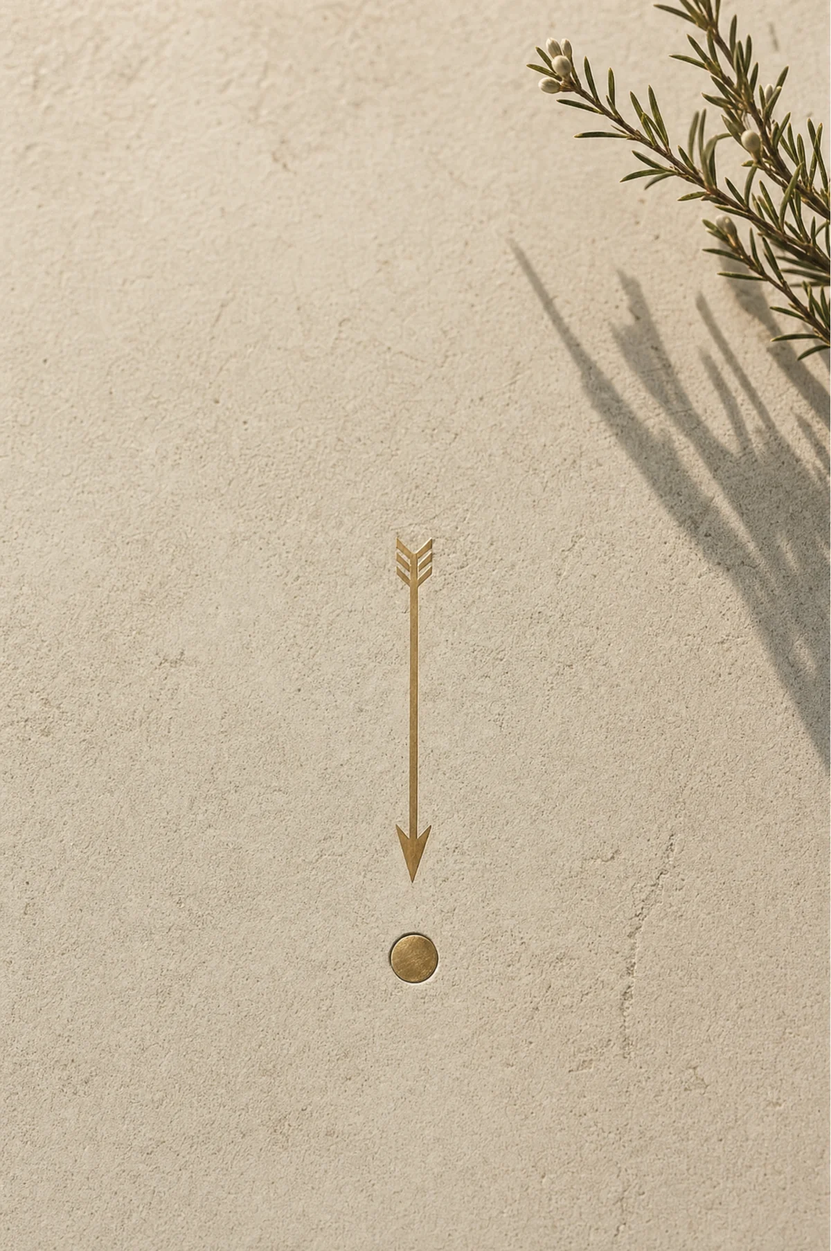 A slim brass arrow inlaid into bone plaster pointing to a single small brass disc set flush into the stone