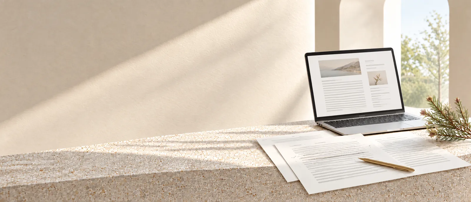 Printed pages of website copy with pencil edits and a brass pen, a laptop showing an article behind, on pale stone