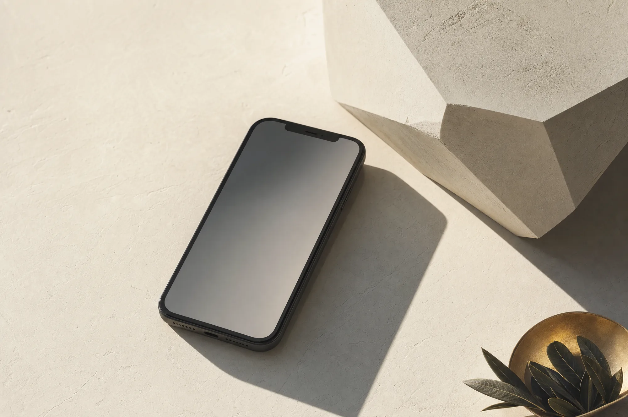 A phone lying face up on bone plaster beside a faceted pale stone block, throwing one long clean shadow